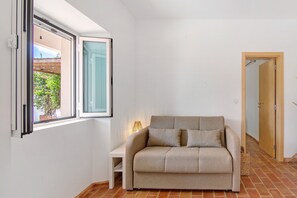 Une pièce avec un canapé, une petite table, une fenêtre et une porte.