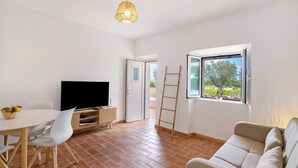 Une pièce avec une télévision, des chaises blanches, une table, un canapé, une fenêtre donnant sur un paysage et une échelle.