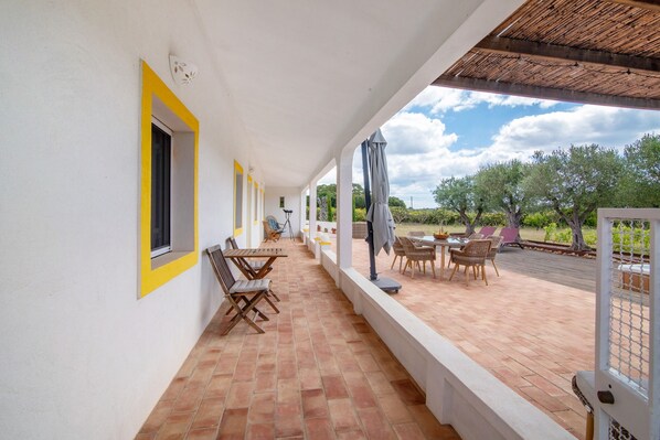 Une terrasse extérieure couverte, avec une table et des chaises, donnant sur le jardin, et une porte dont le cadre est jaune.
