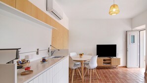 Une cuisine moderne avec des meubles blancs, un coin repas équipé d’un téléviseur et un sol carrelé de carreaux rouges.