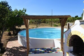 Une piscine surmontée d’une pergola en bois, entourée de verdure.
