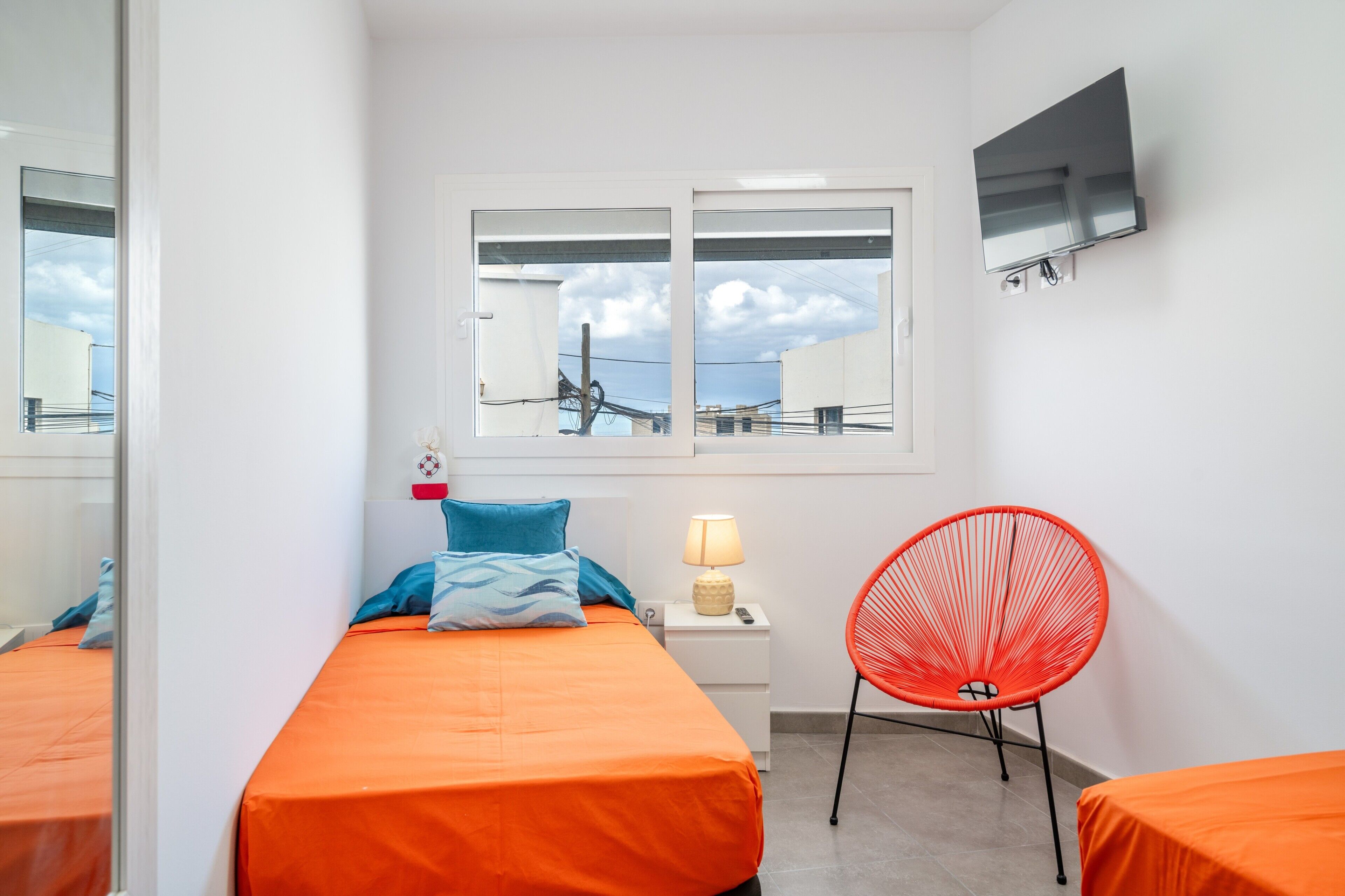 Een kamer met twee bedden, een stoel, een televisie en een raam met uitzicht.