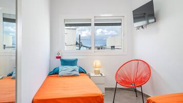 Een kamer met twee bedden, een stoel, een televisie en een raam met uitzicht.