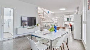 A modern kitchen with a dining area, white cabinetry, a flat-screen TV, and a staircase leading to an upper level. - Vacation Apartment 'Sparrow' with Wi-Fi and Air Conditioning (La Santa)