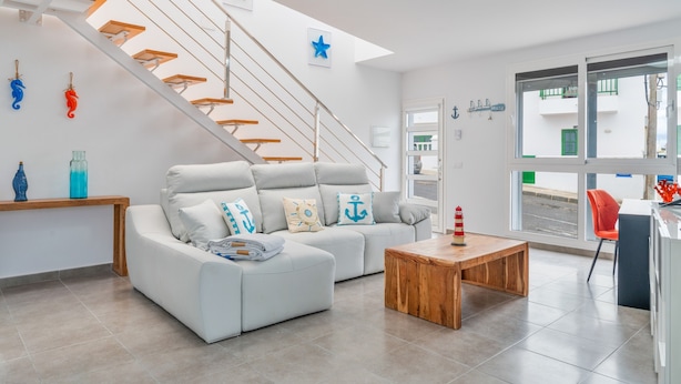 A modern living room with a sofa, wooden coffee table, and a staircase with wooden railings. - Vacation Apartment 'Sparrow' with Wi-Fi and Air Conditioning (La Santa)