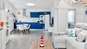 A modern kitchen with blue cabinets, a dining area with a white table and chairs, and a living room with a white sofa and decorative pillows. - Vacation Apartment 'Sparrow' with Wi-Fi and Air Conditioning (La Santa)