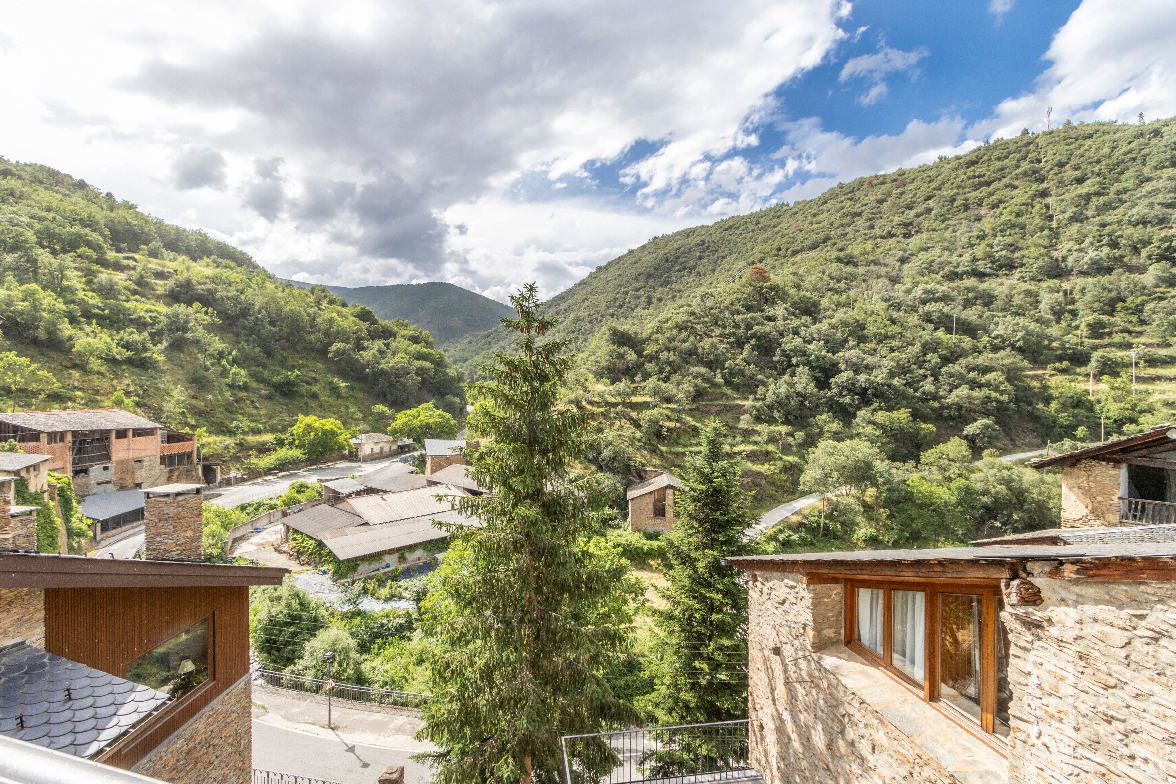A mountainous village with stone buildings, a prominent tree, and a clear sky.