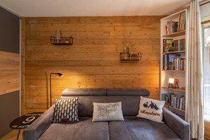 A cozy room with a grey sofa, a bookshelf, and wooden panel walls.