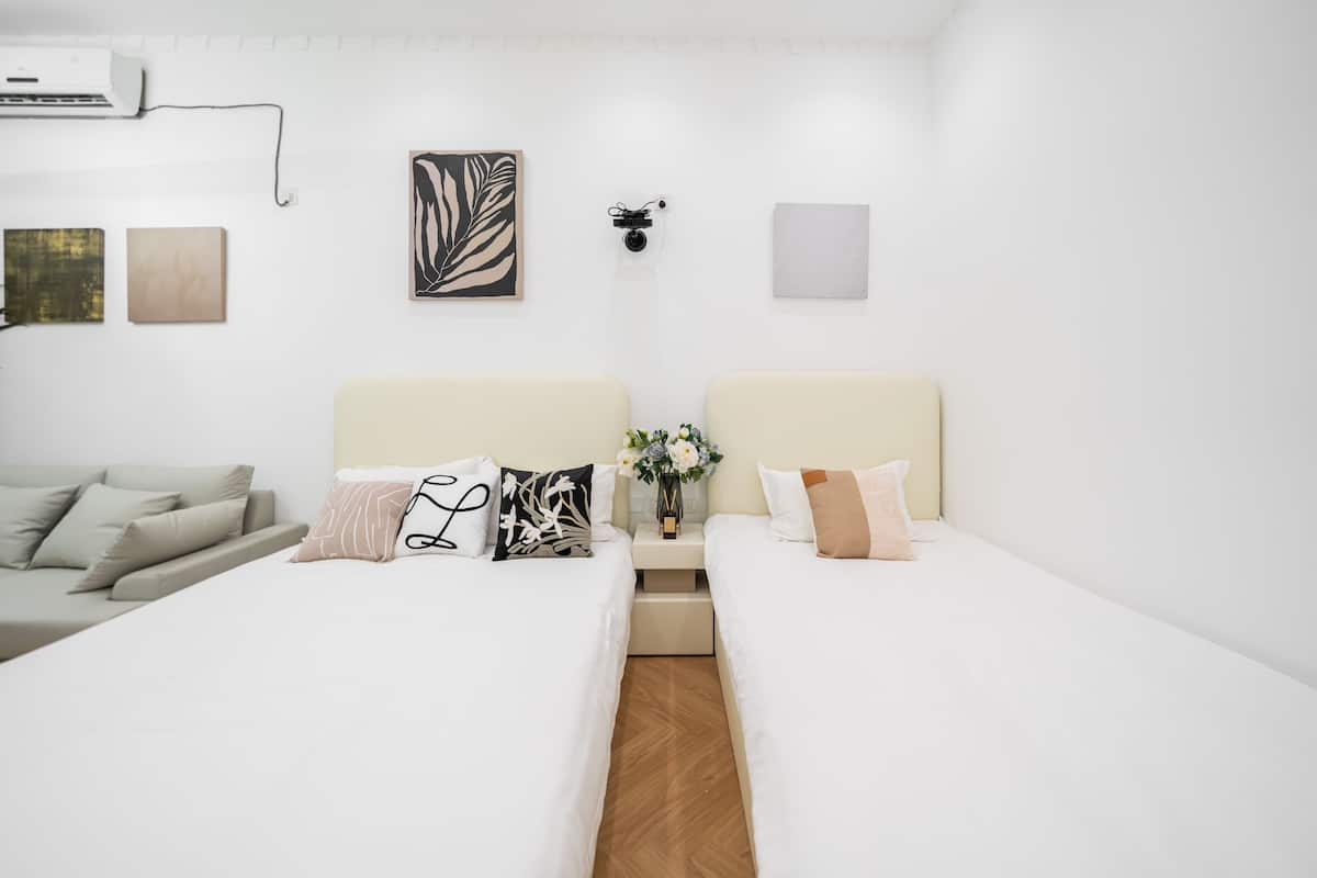 A hotel room with two beds, a sofa, a wall-mounted air conditioner, and artwork.