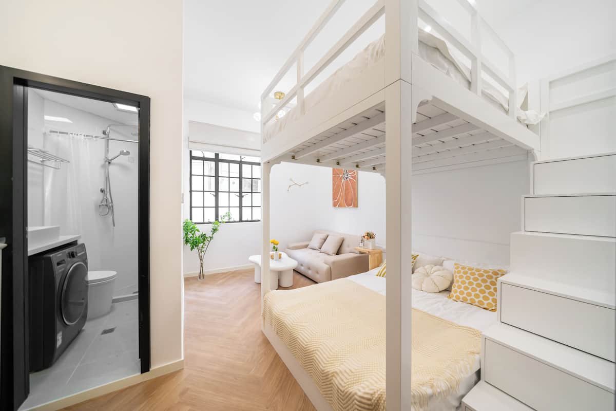 A modern bedroom with a bunk bed, a sofa, a small table, and a shower area.