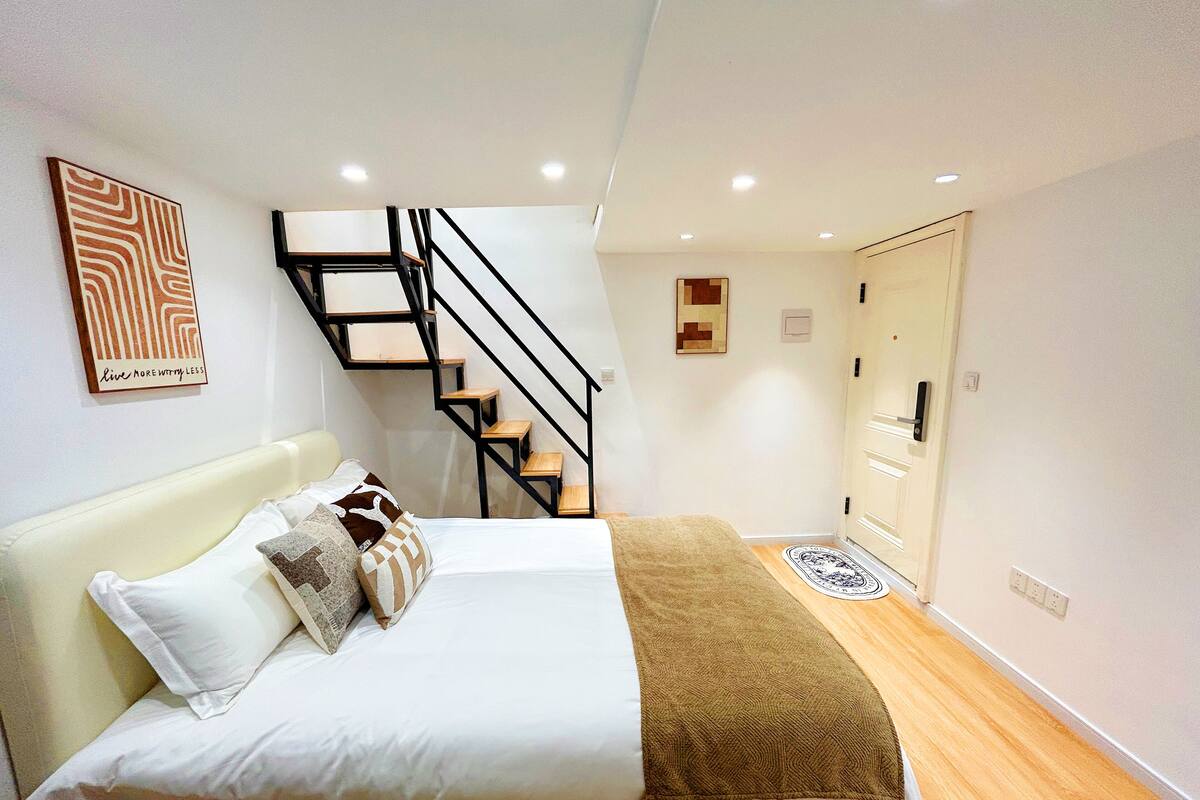 A bedroom with a bed, a staircase, a wardrobe, and a wall with a framed picture.