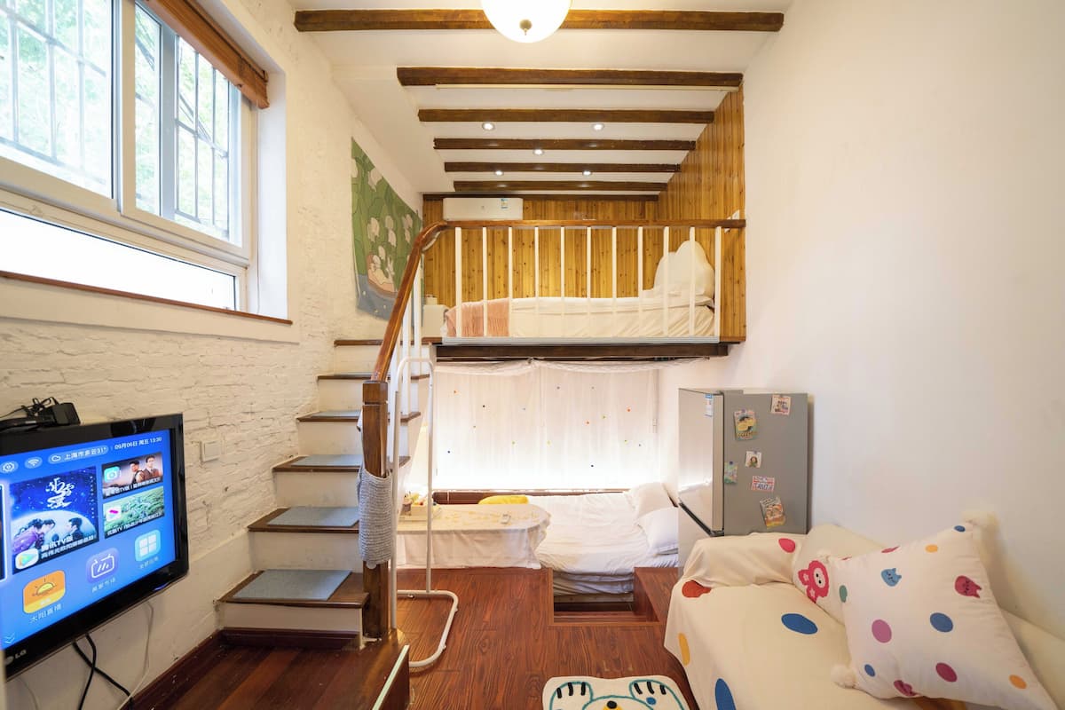 A dorm-style room with bunk beds, a television, a desk, and a refrigerator.