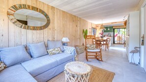 Ein gemütliches Wohnzimmer mit einer Holzwand, einem blauen Sofa, einem runden Spiegel und einem Essbereich mit Holzsesseln.