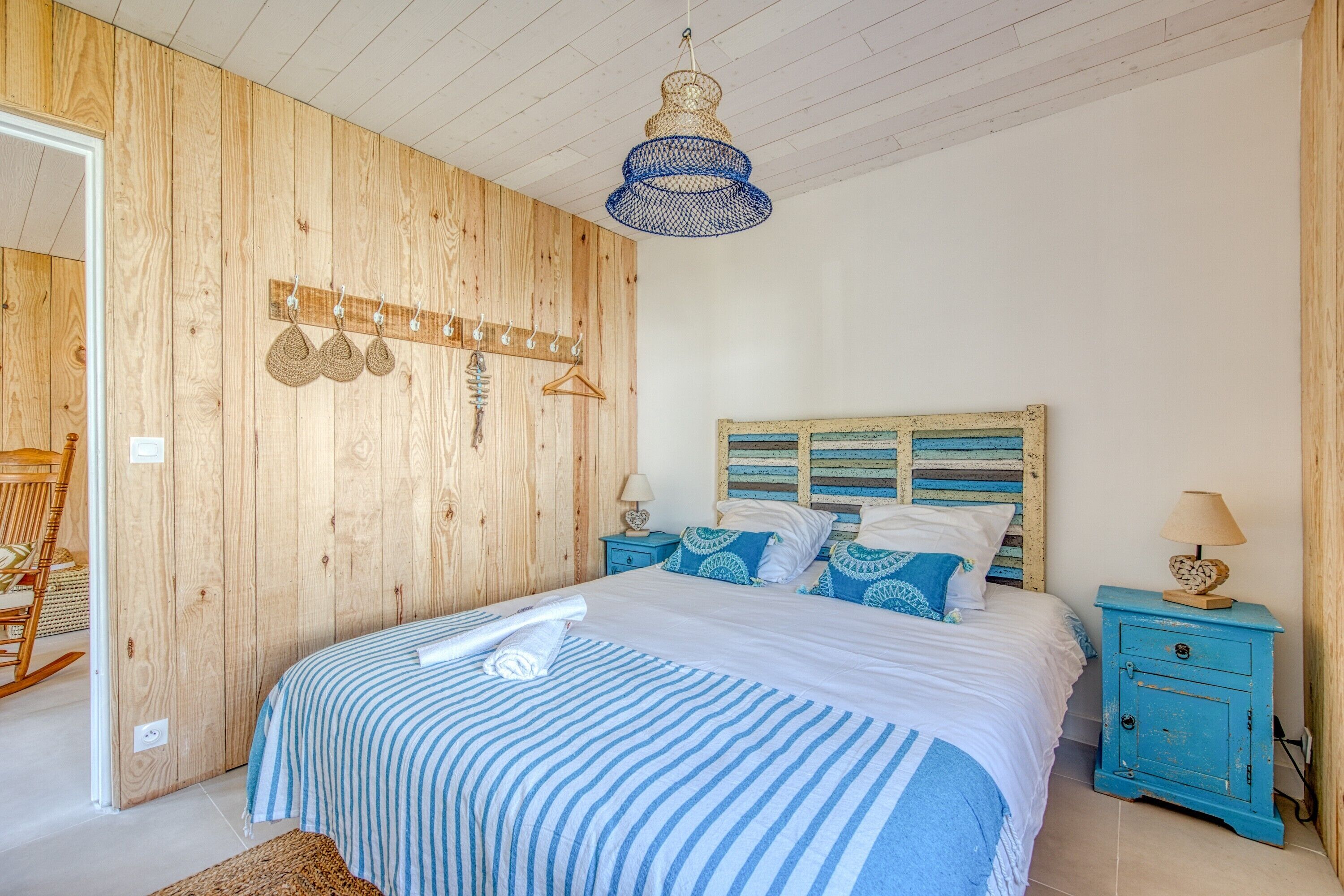 Ein Schlafzimmer mit einer Holzwand, einem Bett mit gestreifter Bettwäsche, einem blauen Nachttisch und einer hängenden Leuchte.