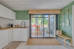 A kitchen with white cabinets, a wooden countertop, a sink, and a view of an outdoor deck with a hammock. - Holiday Home 'De Charme Au Bord Du Lac' with Private Terrace, Garden and Wi-Fi (Hourtin)
