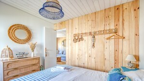 Ein Schlafzimmer mit einer Holzwand, einem Bett mit gestreifter Bettwäsche, einer hängenden Körbot und einem Spiegel.
