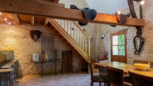 Ein rustikales Interieur mit einer Holztreppe, Steinwänden, einem Essbereich mit einer großen Schüssel und einem Kleiderständer.