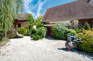 A gravel driveway leading to a house with a tiled roof, surrounded by greenery and a large vase. - Cottage 'Gite Soleil' with Shared Pool, Private Terrace and Wi-Fi (Degagnac)