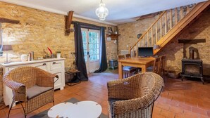 Un intérieur rustique avec des murs en pierre, des meubles en osier, un escalier en bois et une cheminée traditionnelle.