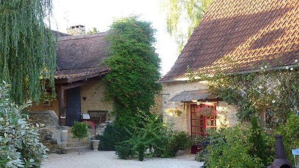 Une cour avec un chemin de gravier, un mur en pierre et un bâtiment doté d’un toit en tuiles.