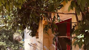 Un bâtiment rustique avec une porte rouge, entouré d’une végétation luxuriante et de plantes en fleurs.