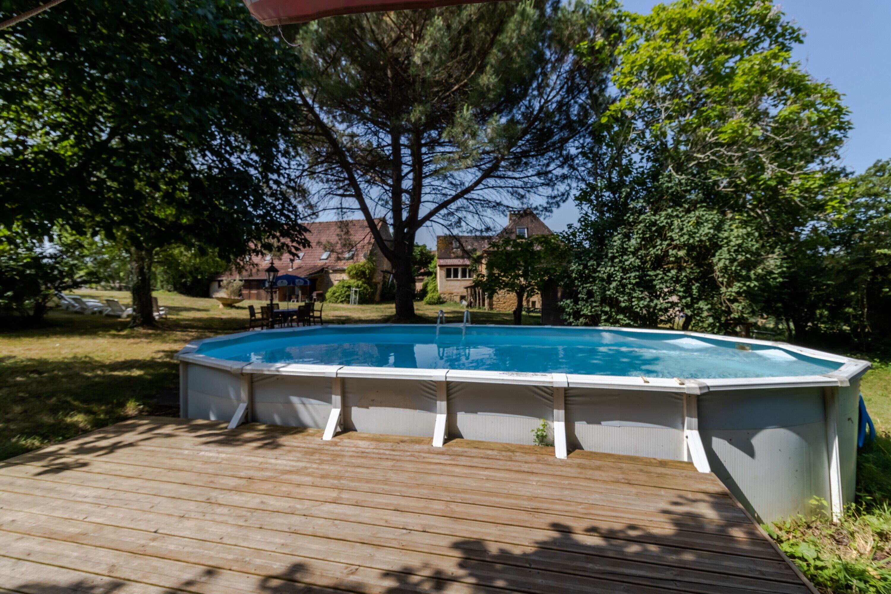 A rectangular above-ground pool with a wooden deck, surrounded by trees and houses in the background.