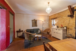 A cozy living area with a sofa, wicker chairs, a dining table, and a stone wall. - Cottage 'Gite Lune' with Shared Pool, Private Terrace and Wi-Fi (Degagnac)