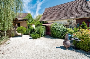 A gravel driveway leading to a house with a tiled roof, surrounded by greenery and a large vase. - Cottage 'Gite Lune' with Shared Pool, Private Terrace and Wi-Fi (Degagnac)