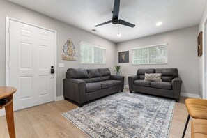 A living room with two dark sofas, a patterned rug, a ceiling fan, and a white door.