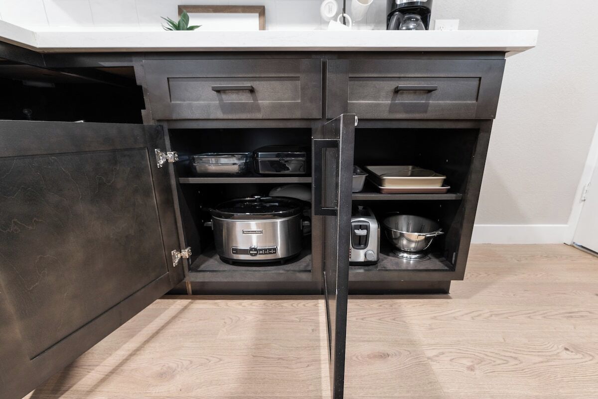A kitchen with a dark cabinet, a toaster, a slow cooker, and a coffee maker on the countertop.