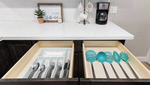 A kitchen counter with a coffee maker, mugs, and a sign that says 'Life Happens. Coffee Gel.' Below, there are two drawers with utensils and kitchen tools. - The General Sherman Cabin Sequoia Motel (Three Rivers)