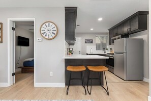 Une cuisine moderne avec un îlot central, des tabourets de bar, une horloge et un réfrigérateur.