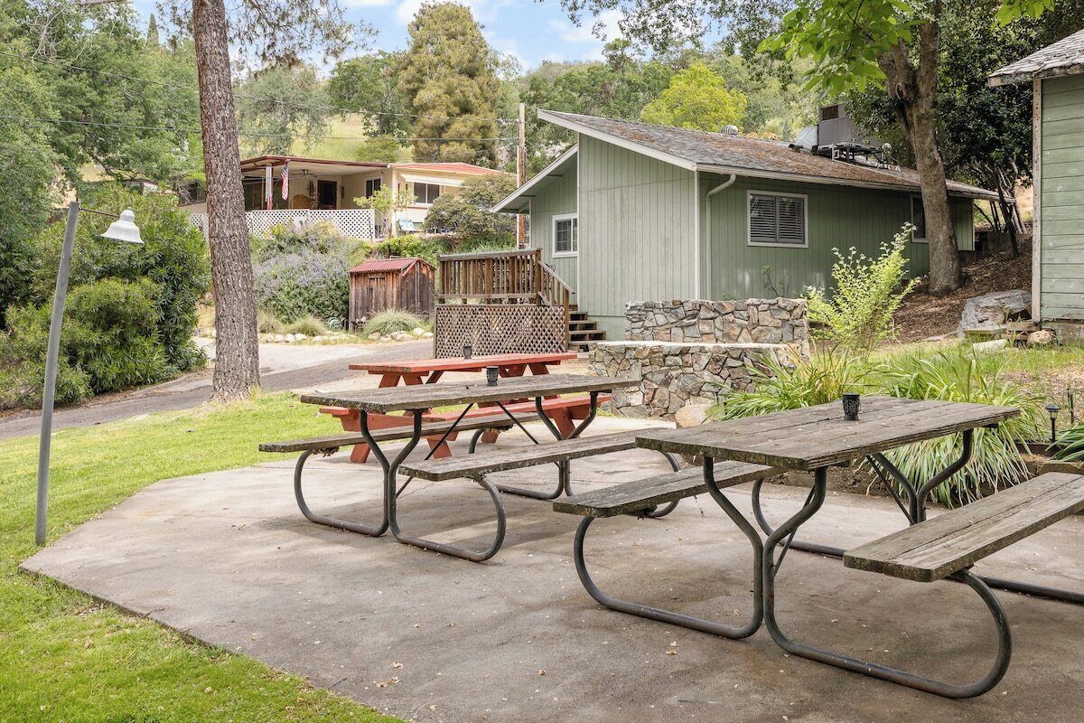 Una mesa de picnic sobre un patio de concreto con un muro de piedra y una terraza de madera al fondo.