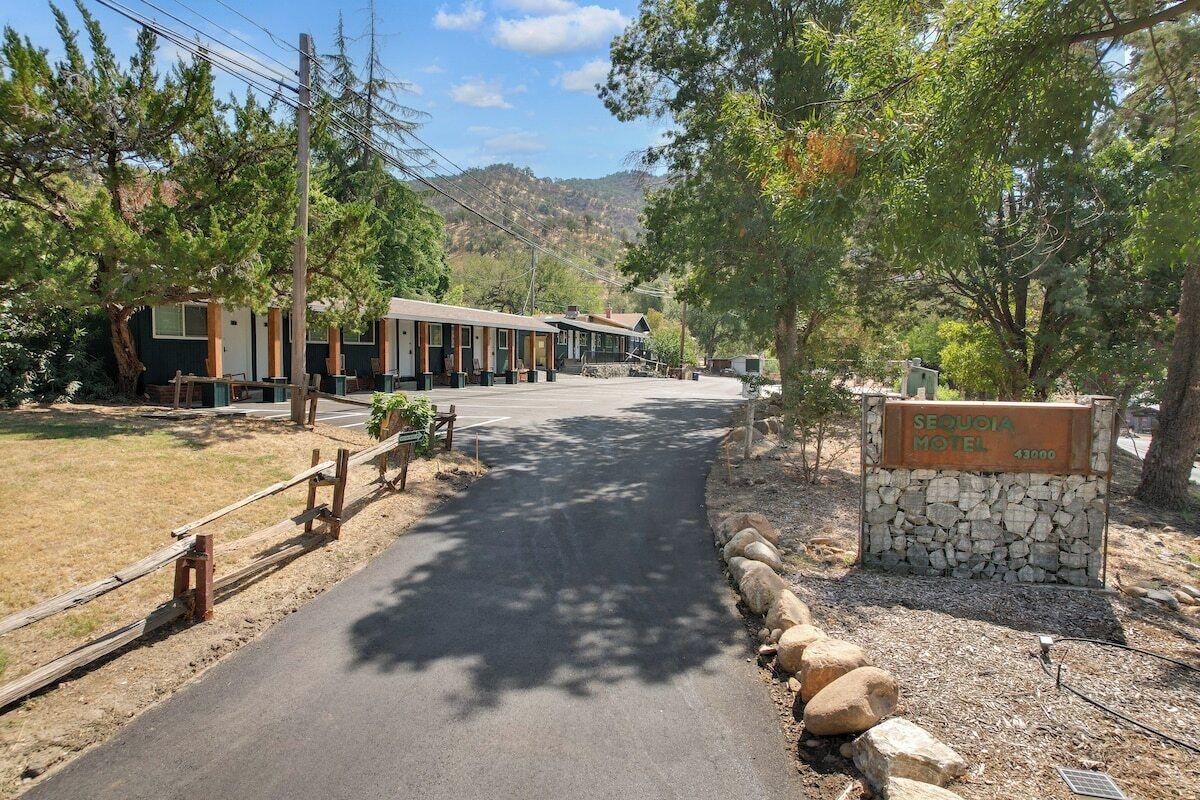 A motel with a paved driveway leading to the entrance, surrounded by trees and a mountainous backdrop.