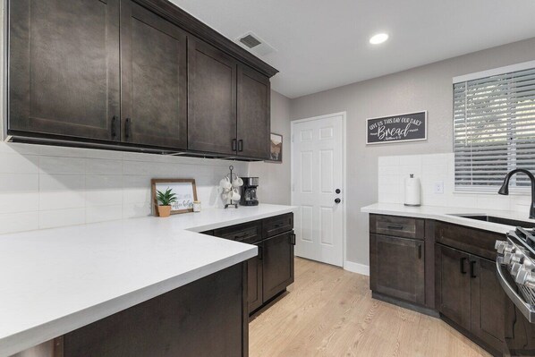 A kitchen with dark cabinets, a white countertop, and a window with blinds.