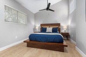 A bedroom with a bed, ceiling fan, bedside lamps, and a window with blinds.