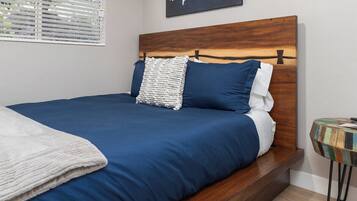 A neatly made bed with a wooden headboard, a world map on the wall, and a small round table with a colorful top.