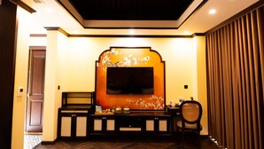 Una sala de estar con un televisor de pantalla plana montado en la pared, detalles decorativos, un mueble de madera con un tablero de ajedrez y una silla.