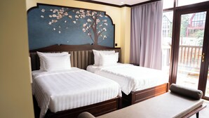 Habitación de hotel con dos camas, un banco y un ventanal con cortinas.