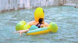 Una persona flota sobre una balsa hinchable amarilla y verde en una piscina con una cascada al fondo.