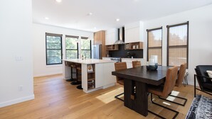 A modern kitchen with a central island, wooden flooring, and large windows. - Alpine Nest Bridger Bowl A (Bozeman)