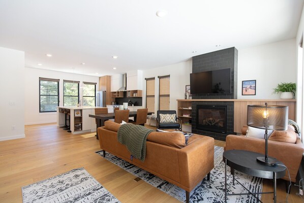 A modern living room with a sofa, coffee table, and fireplace. There is a dining area with a table and chairs.