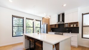 A modern kitchen with a central island, bar stools, and large windows. - Alpine Nest Bridger Bowl A (Bozeman)