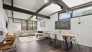 A modern living room with a dining area, featuring a large window, a ceiling fan, and a map on the wall. - Stylish Home near Love-Field Airport, King & Queen Beds with a Large Yard (Dallas)