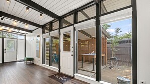 A spacious room with large windows, a wooden floor, and a green bench. - Stylish Home near Love-Field Airport, King & Queen Beds with a Large Yard (Dallas)