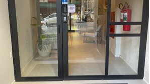 A modern entrance with glass doors, a digital visitor sign, and a 'NEXT REALTY' mat. - Jardim Paulista Studio Completo (Jardim Paulista São Paulo)