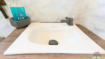 A white bathroom sink with a single faucet, a soap dispenser, and a stone basin.