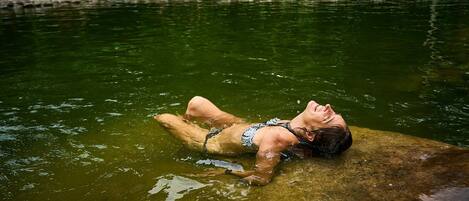 A person lying on a rock in a body of water surrounded by greenery.