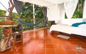 A bedroom with a bed, a hammock, a small table, and a view of greenery. - ARIANTIY HOSTAL (Mocoa)