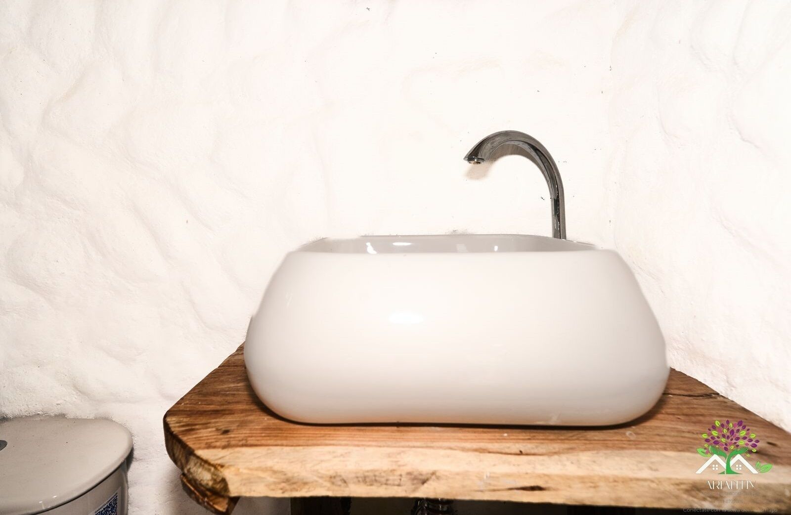 A white ceramic sink with a curved faucet on a wooden countertop.